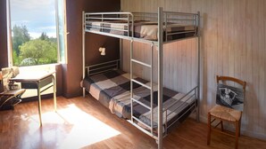 Una cama litera con escritorio y silla, una ventana con vista a árboles, y una pared de madera.