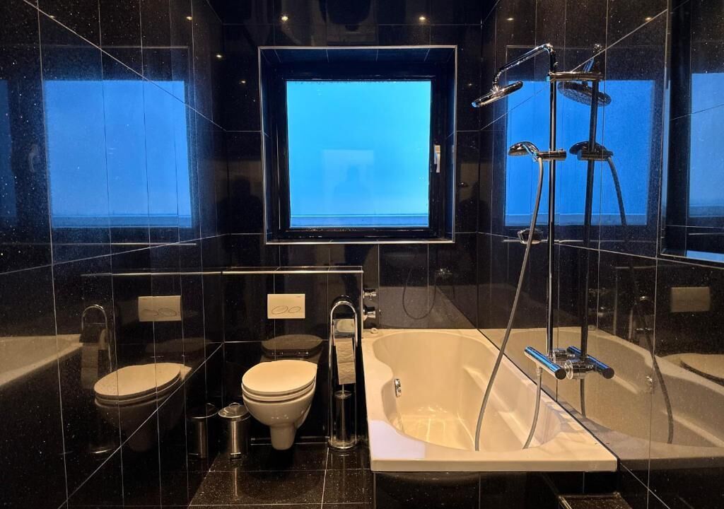 Ein modernes Badezimmer mit einer Badewanne, zwei Toiletten, einer Dusche und einem großen Spiegel.