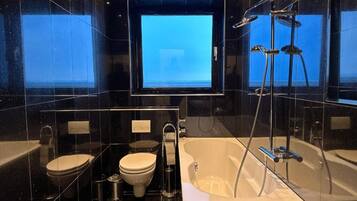 Ein modernes Badezimmer mit einer Badewanne, zwei Toiletten, einer Dusche und einem großen Spiegel.