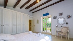 Un dormitorio con cama, escritorio, silla, armario y ventana con vista a follaje.