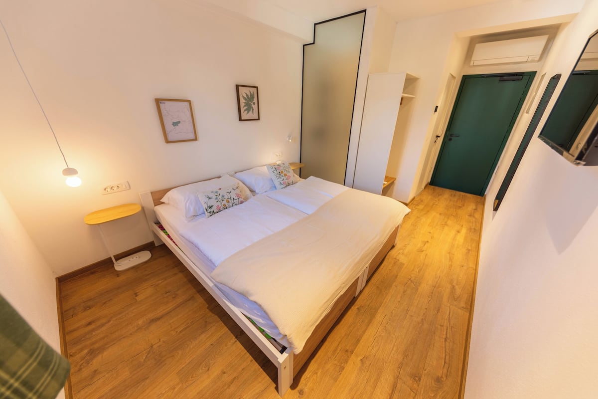 A bedroom with a bed, bedside table, wall art, and a mirror.