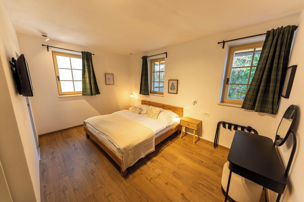 A bedroom with a bed, bedside table, chair, and a television on the wall.