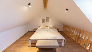 A bedroom with a large bed, a bench, wooden flooring, a sloped ceiling, and a wooden railing. - Hotel Old Coach House (Bled)