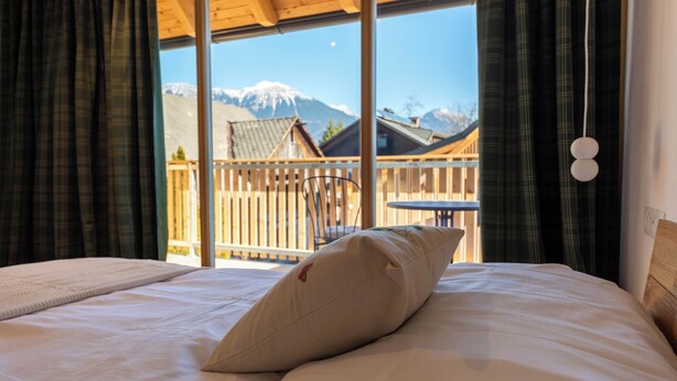 A bed with a pillow, a view of a wooden balcony, and a mountain in the background. - Hotel Old Coach House (Bled)