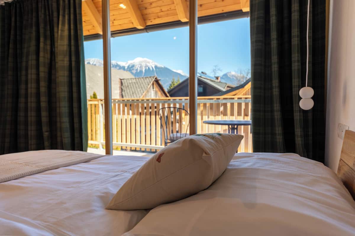 A bed with a pillow, a view of a wooden balcony, and a mountain in the background.