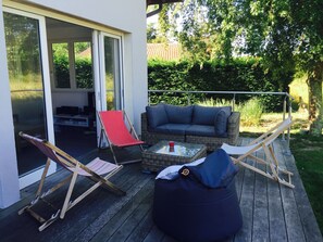 A deck with a wicker sofa, a red and white striped beach chair, a blue bean bag, and a glass coffee table.