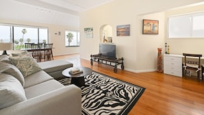 Een woonkamer met een bank, salontafel, een zebra vloerkleed, een tv op een karretje, een eethoek en kunstwerken aan de muur.