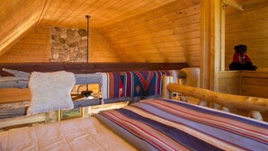 Un chalet confortable aux murs en bois et au plafond en pente, agrémenté d’un mur en pierre, d’une cheminée et d’un lit recouvert d’une couverture aux couleurs vives.