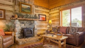 L’intérieur d’un chalet rustique, avec une cheminée en pierre, des meubles en cuir et une grande fenêtre.