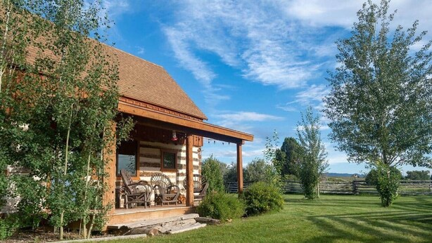 Une cabane en rondins avec un porche, un espace salon extérieur et une pelouse bien entretenue.