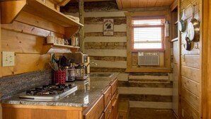 Une cuisine rustique avec des murs en bois, un plan de travail en granit et une fenêtre équipée de stores.