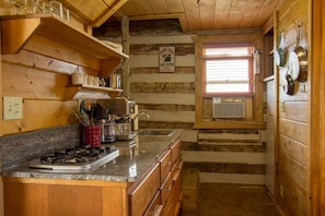 Une cuisine rustique avec des murs en bois, un plan de travail en granit et une fenêtre équipée de stores.