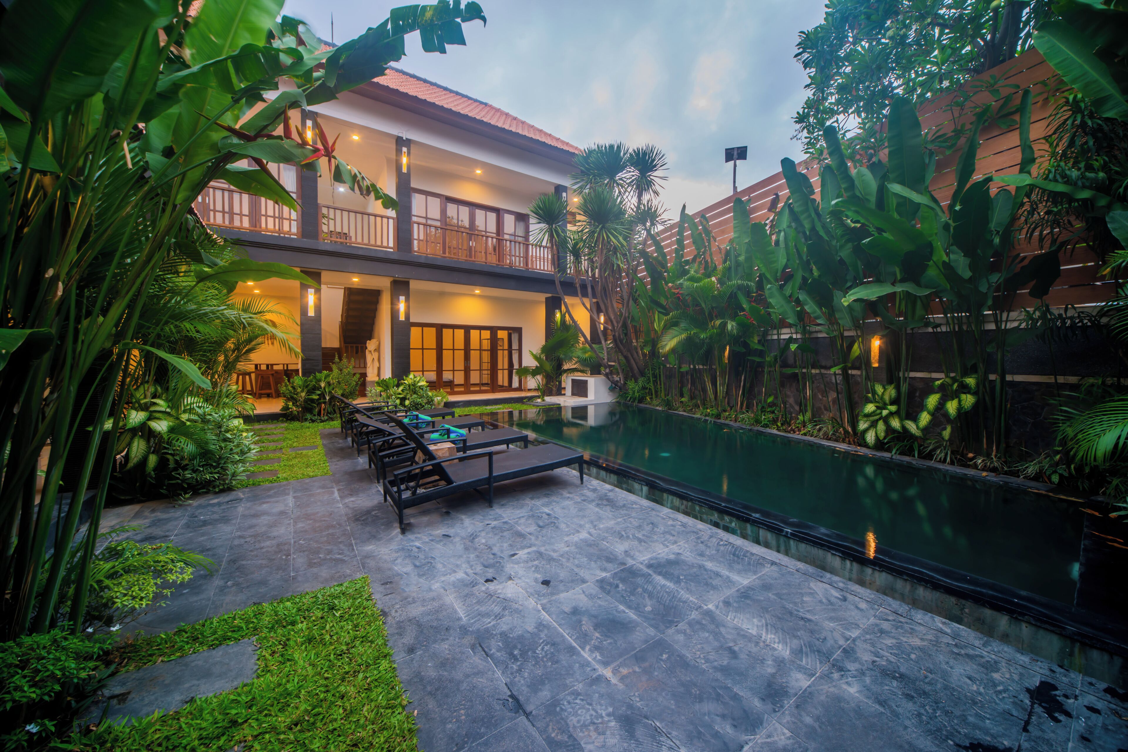 A two-story building with a swimming pool, outdoor seating, and lush greenery.