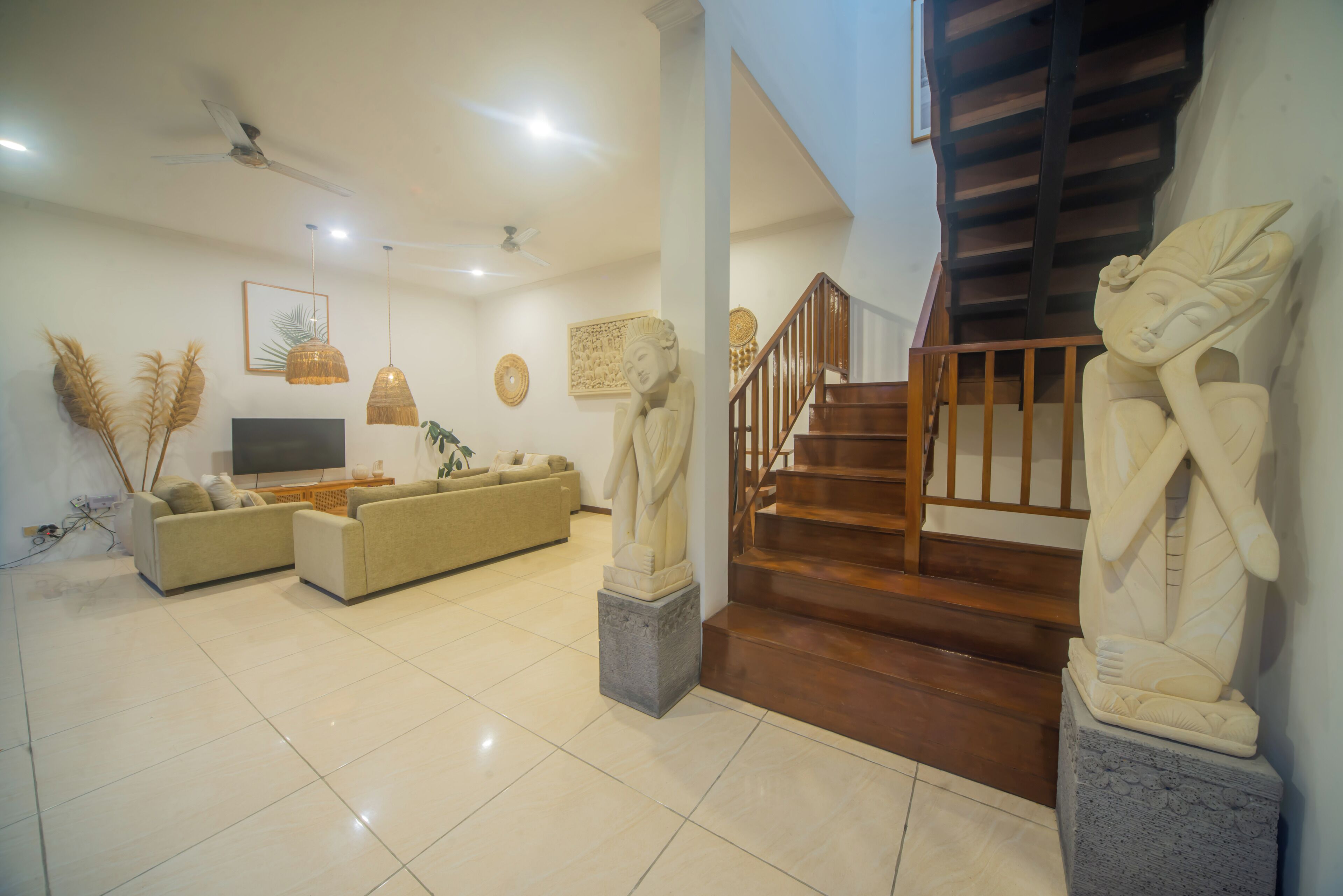 A spacious living room with a sofa set, a flat-screen TV, decorative wall art, and a staircase with wooden railings.