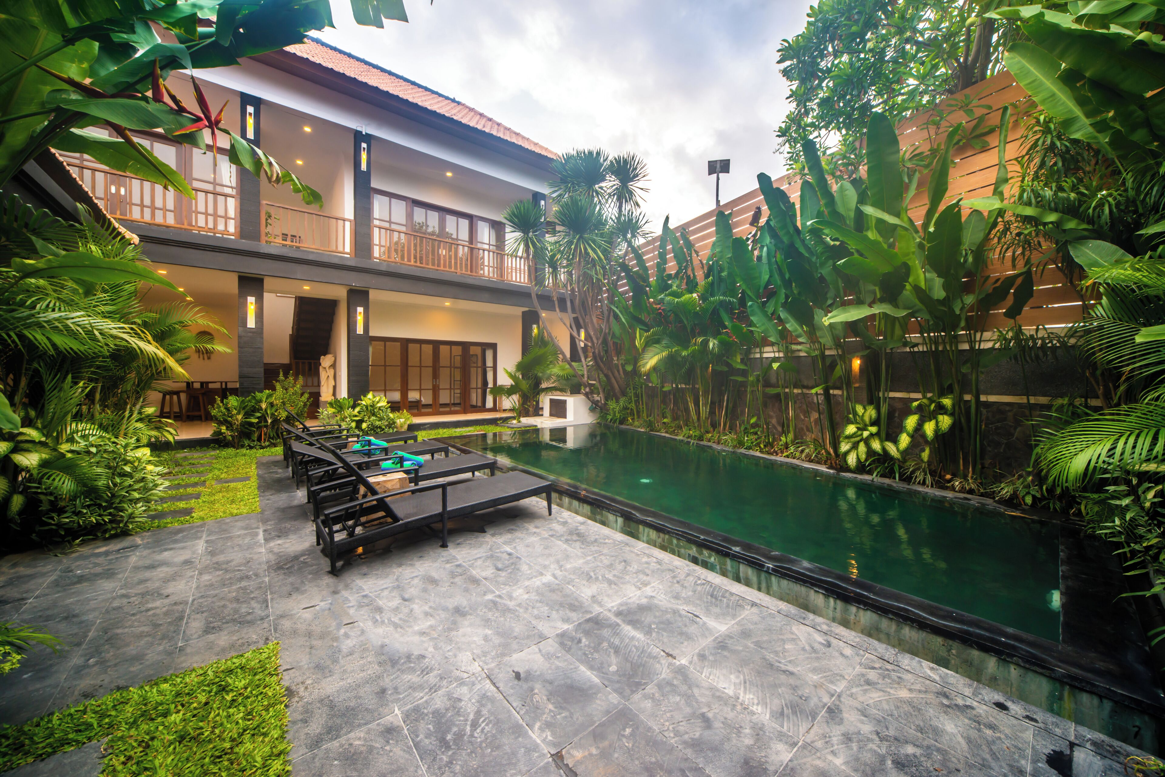 Um edifício de dois andares com piscina, área de estar externa e vegetação exuberante.