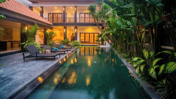 A two-story building with a swimming pool, lounge chairs, and tropical plants. - 3BR Villa White Rose Central Canggu (Canggu)