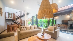 A spacious living area with a sofa set, two round coffee tables, a staircase, and a view of a garden. - 3BR Villa White Rose Central Canggu (Canggu)