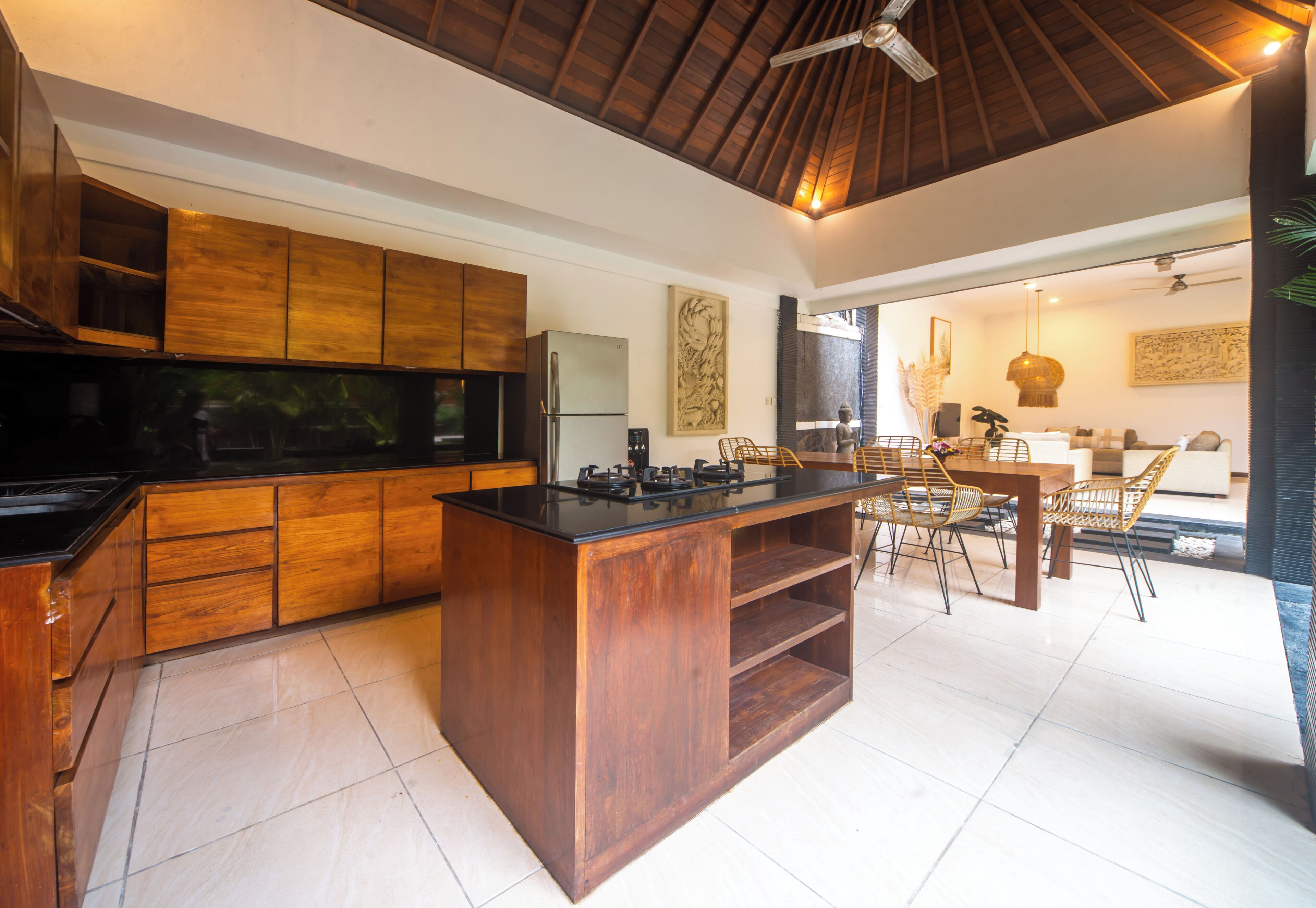 Una cocina moderna con armarios de madera, encimera negra y un comedor con sillas de mimbre.