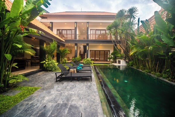 A two-story building with a swimming pool, outdoor seating, and lush tropical plants. - 3BR Villa White Rose Central Canggu (Canggu)