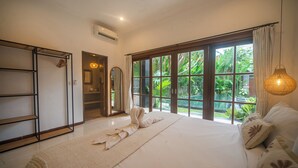 A bedroom with a large bed, a wardrobe, a mirror, and a view of greenery through the window. - 3BR Villa White Rose Central Canggu (Canggu)