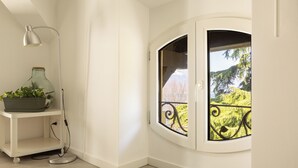 A corner room with a white wall, a window with a black iron railing, a white floor, a white desk with a lamp, and a green plant on the desk. - Elegant Lakefront Penthouse - Casa Barozzi (Luino)