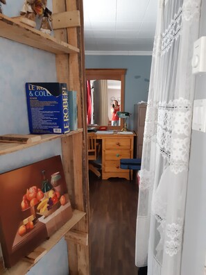 A room with a wooden desk, a chair, a mirror, a bookshelf with books, and a painting.