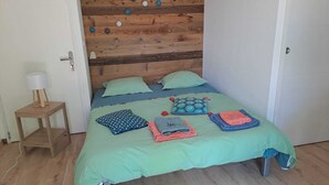 A bed with a wooden headboard, a bedside table with a lamp, and a small stool. - Studio NATURE (Marboz)