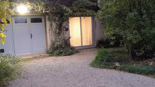 A gravel driveway leading to a building with a sliding glass door and a white garage door. - Studio NATURE (Marboz)