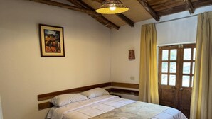 Ein Schlafzimmer mit einem Holzbett, einem gerahmten Bild an der Wand, einem Fenster mit Vorhängen und einer Holzbalkendecke.