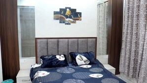 Ein Schlafzimmer mit einem Bett, einem Nachttisch, einem Wandbild und einem Fenster mit Vorhängen.