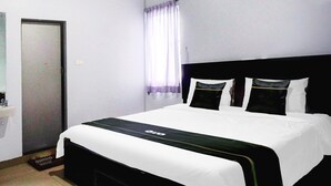 Hotellihuone, jossa on sänky, ovi, ikkuna, jossa on verhot, ja pieni pesuallas.