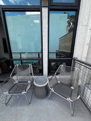 A balcony with two metal chairs and a small round table, overlooking a pool area.
