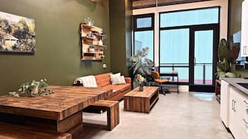 A modern living space with a large wooden dining table, a sofa, and a kitchen area.