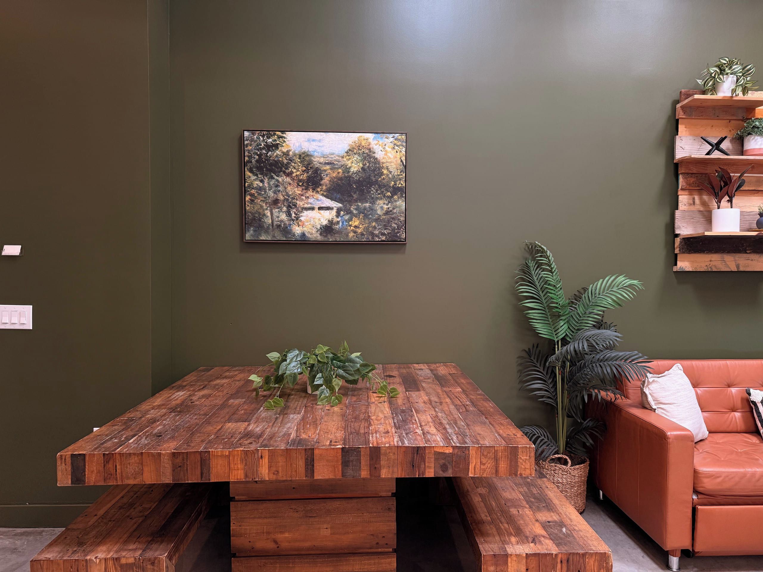 Una habitación con una mesa de madera, un cuadro en la pared, una planta en maceta y un sofá.