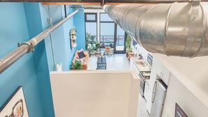 A modern kitchen with a large stainless steel range hood, a dining area with a wooden table and chairs, and a blue wall with a framed picture. - Stylish Downtown Loft Near Disney (Santa Ana)