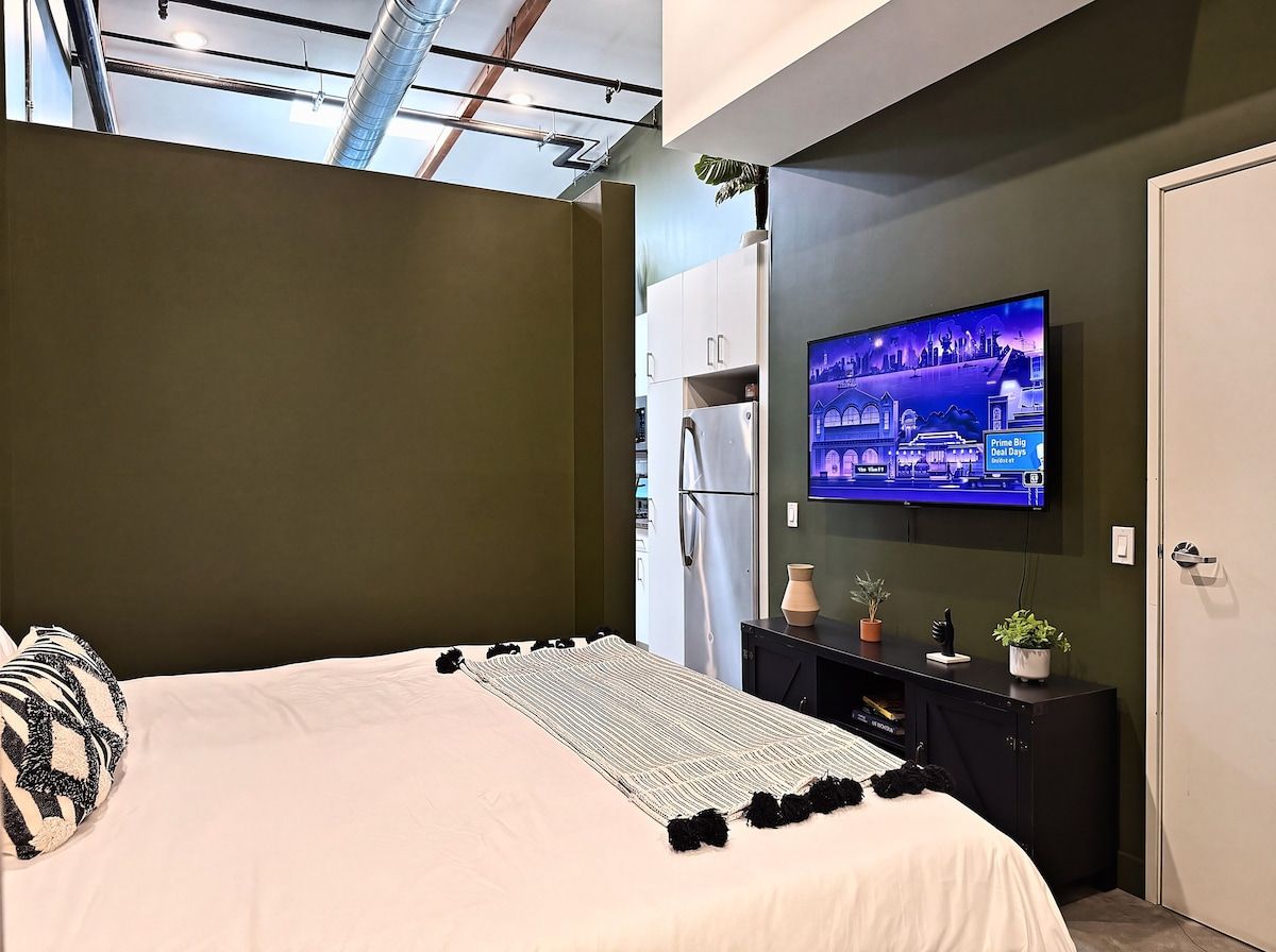 A modern hotel room with a bed, a flat-screen TV, a small desk, and a door.