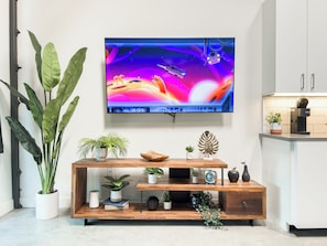 Un salon moderne avec un téléviseur à écran plat fixé au mur, une console en bois agrémentée de divers objets décoratifs et de grandes plantes vertes.