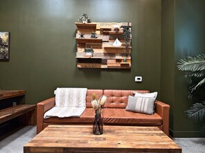 A room with a brown leather sofa, a wooden coffee table, and a wall-mounted wooden shelf with decorative items. - New Design -Downtown Loft Near Disney & John Wayne (Santa Ana)