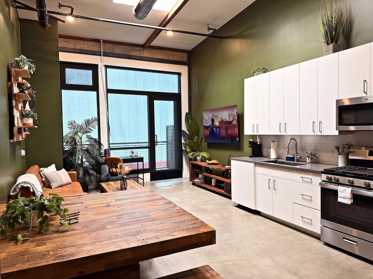 A modern kitchen with white cabinets, a wooden dining table, and a large window.