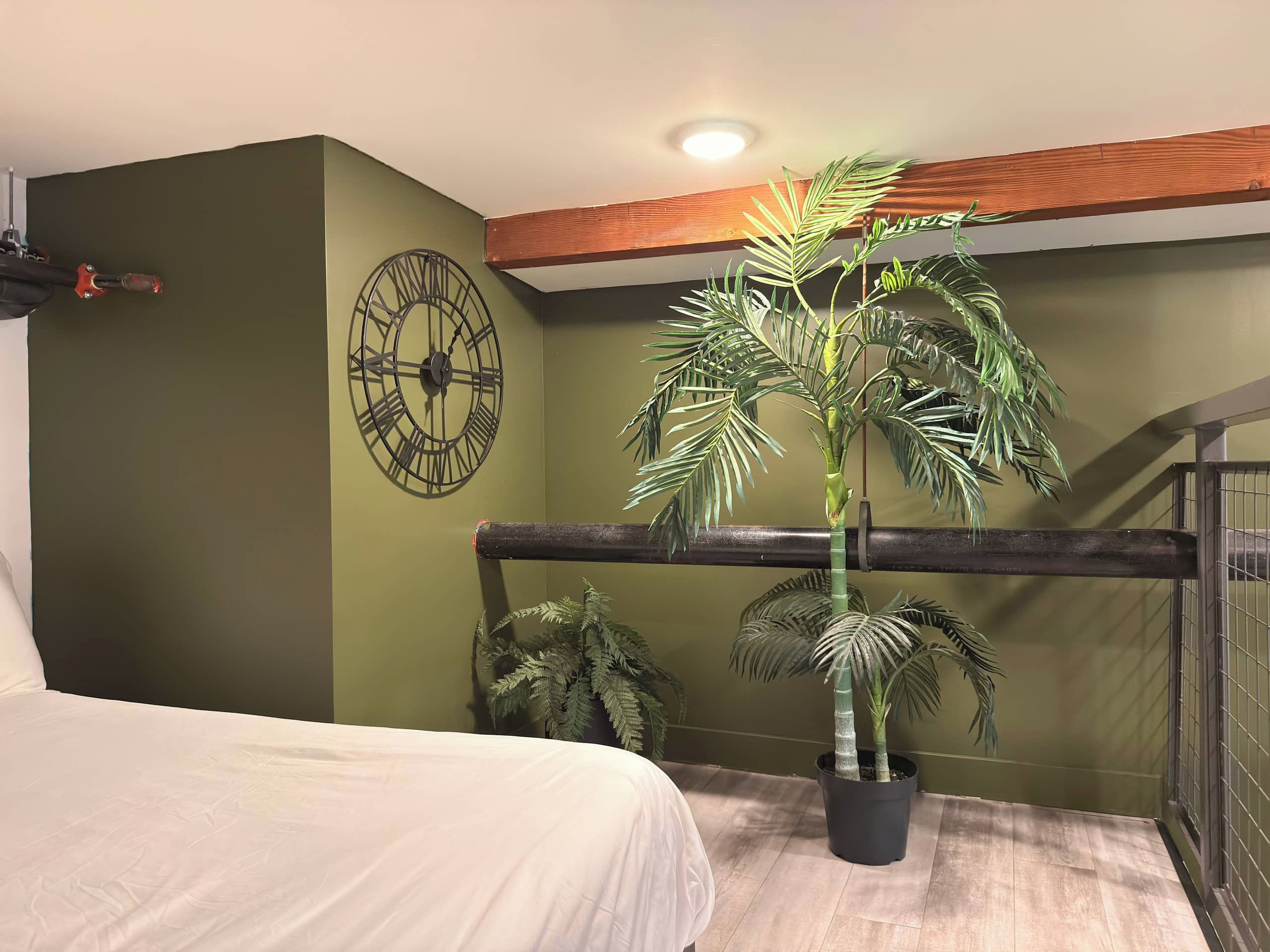 A bedroom with a bed, a large wall clock, and a potted palm plant.
