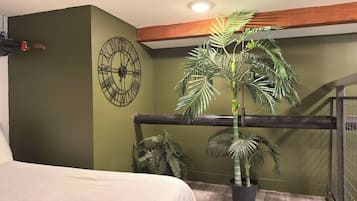 A bedroom with a bed, a large wall clock, and a potted palm plant.
