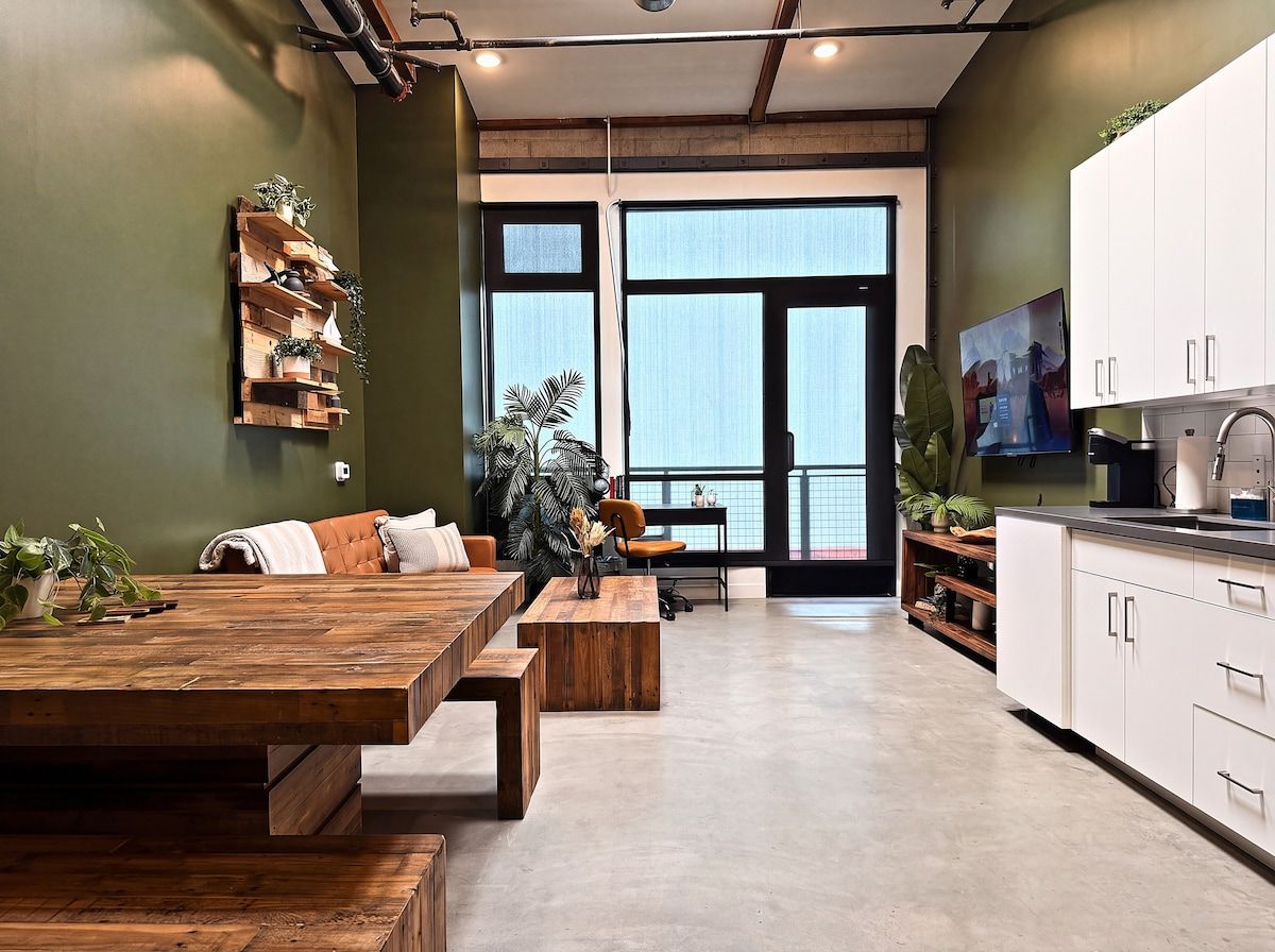 A modern kitchen with white cabinets, a wooden dining table, and a large window.