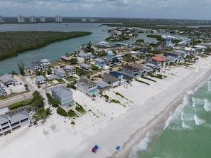 An aerial view of a coastal residential area with beachfront properties, a marina, and a distant view of high-rise buildings. - Bonita Beach & Bay Views | 200 Steps to the Beach (Bonita Springs)