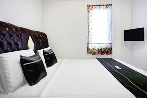 Une chambre d’hôtel avec une tête de lit capitonnée, du linge de lit blanc, des oreillers noirs, un rideau à motifs floraux et un téléviseur à écran plat fixé au mur.