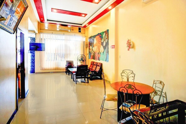 A hotel lobby with a long corridor, a dining area with metal chairs and a round table, and a large floral mural on the wall.