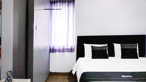 Une chambre d’hôtel avec un lit, une fenêtre avec des rideaux, une table de chevet et une étagère fixée au mur.