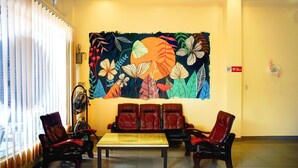 Un vestíbulo con un gran mural en la pared, una zona de estar con sillones de cuero, un ventilador y una mesa.