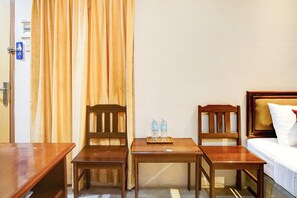 Une chambre d’hôtel avec un lit, deux chaises en bois, une petite table avec des bouteilles d’eau et une porte avec une pancarte.