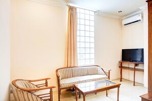A living room with a sofa, two armchairs, a coffee table, a TV on a stand, and a window with curtains.