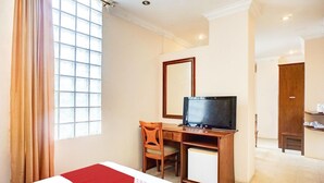 Una habitación de hotel con una cama, un escritorio con televisor, una silla y un espejo.